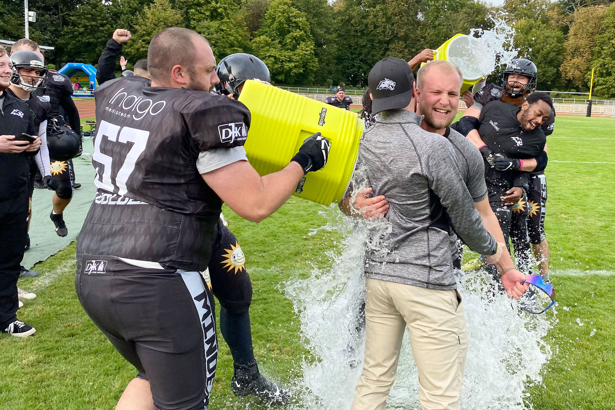 Doppelpack! O-Liner Alexander Gonschor verpasst Offense-Coordinator Danny Wilkening und Defense-Coordinator Eric Wichmann die obligatorische Meister-Dusche. Im Hintergrund ergeht es Headcoach Phil Gamble nicht anders. Foto: DJK Dom Minden